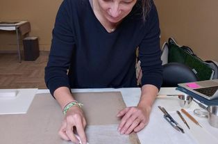 Marine Letouzey, restauratrice d'arts graphiques, consolide le dos d'une académie d'homme